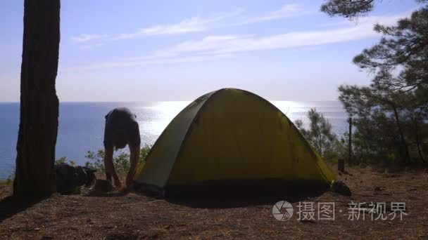 一位男性游客在一座松树林陡峭的海滨海岸的边缘上布置了一座帐篷  海景的壮丽景色。4k