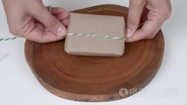 用天然棕纸包裹的天然肥皂的特写。女人的手折叠的角落, 包在包裹周围的字符串, 做一个弓