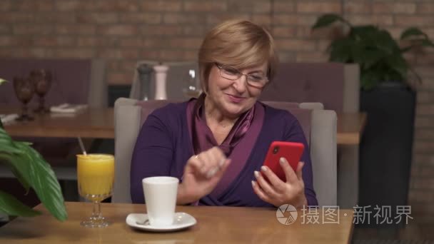 一个可爱的中年妇女坐在咖啡馆里, 看着电话, 滚动手机, 微笑着笑着的特写镜头