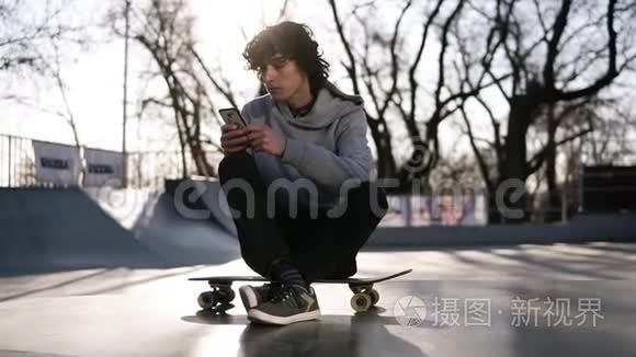 年轻人正拿着手机坐在滑板公园的溜冰区。 一个人正在聪明的人上网
