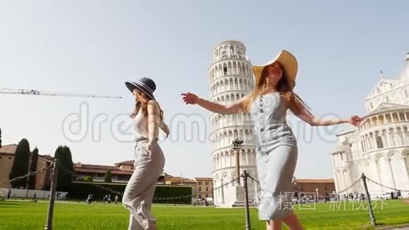意大利比萨。 两个年轻快乐的女人在一个光明的日子里在比萨斜塔的背景上散步
