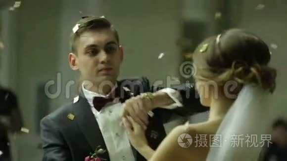 美丽的黑发新娘和英俊的新郎在被纸屑笼罩的婚礼晚会上跳舞。 非常招标