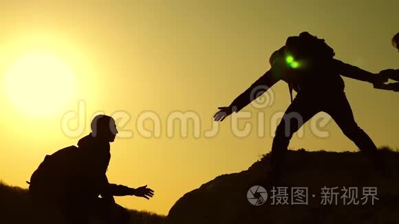 协作登山旅行者在日落。 攀登到山顶的人的剪影。 旅行者爬一个