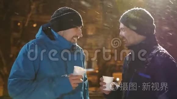 冬天的晚上，两个男人在街上聊天喝咖啡。 下雪了。