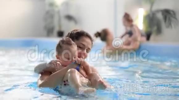 年轻的妈妈在游泳池里慢动作地和她的小女儿玩耍。 积极生活方式的体育家庭
