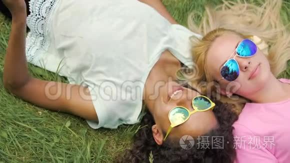 两个女孩最好的朋友躺在草坪上，用手机拍照，在公园里玩得很开心