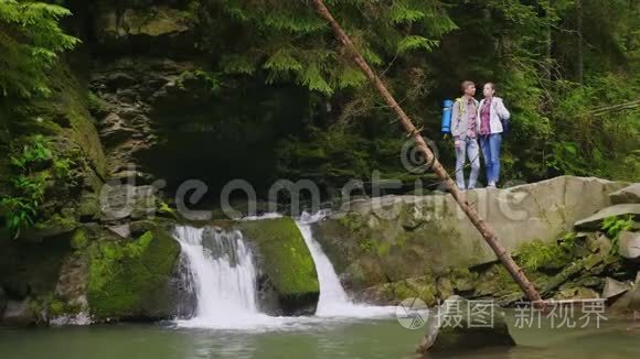 一对年轻的游客正站在山河上的瀑布附近。 欣赏美景.. 旅游业和旅游业