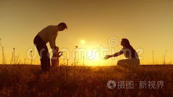 年轻的父母教孩子在金色的夕阳下用脚走路。