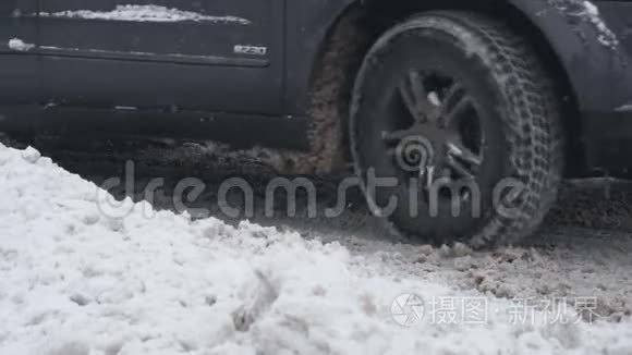 在下雪的白天，带冬天轮胎的越野车在雪道上行驶。 慢动作的车轮特写.. 恶劣天气