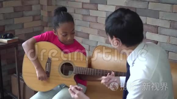年轻的亚洲男老师给非裔美国女孩上吉他课，教她弹吉他