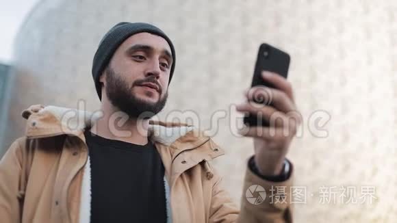 快乐的年轻胡须男有视频聊天，拿着智能手机摄像头和朋友聊天。 外部