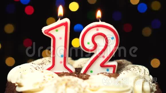 12号在蛋糕上12岁生日蜡烛燃烧在最后吹灭。 彩色模糊背景