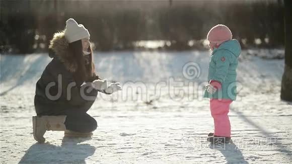 穿着暖和的衣服笑的女人正在向穿着雪衣的女儿扔雪。 母亲和孩子享受寒冷的阳光