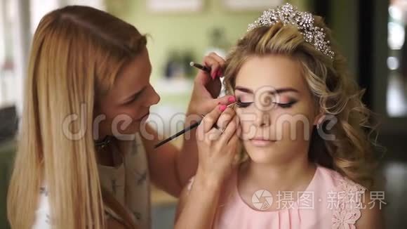 化妆师在一个美丽的沙龙里画新娘的脸。 为年轻健康的女性化妆