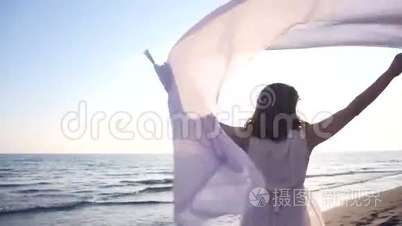 美丽的女人拿着轻盈的布料在海滩上享受日落