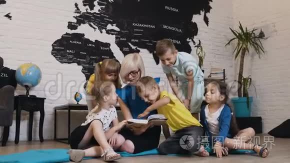 一群漂亮的孩子在幼儿园和幼儿园老师谈论书。 快乐的儿童日托工作者