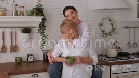 一幅幸福的老母亲和女儿在厨房里的画像，他们喝茶。