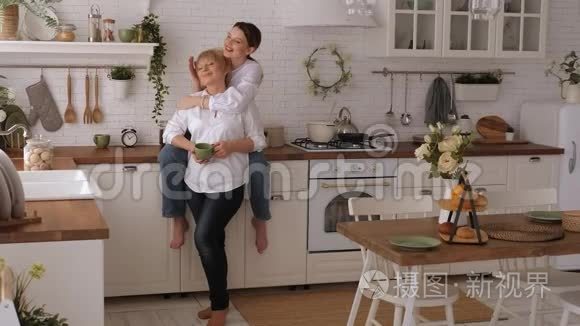 一幅幸福的老母亲和女儿在厨房里的画像，他们喝茶。
