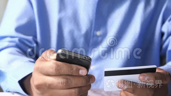 男人`手拿着信用卡，用智能手机上网购物