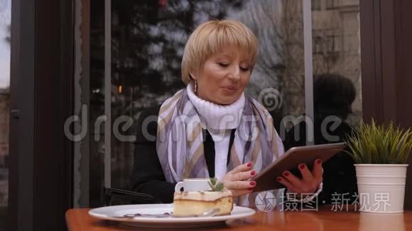 一位年长的商务女士坐在一家带咖啡和平板电脑的街头咖啡馆里。