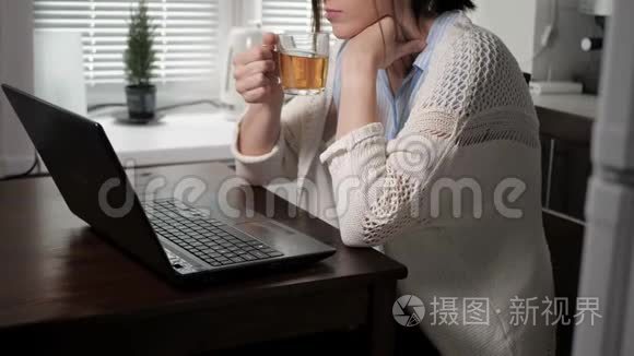 戴着眼镜和针织毛衣的可爱的白种人女孩在厨房里，坐在公寓里，喝着茶，喝着茶。