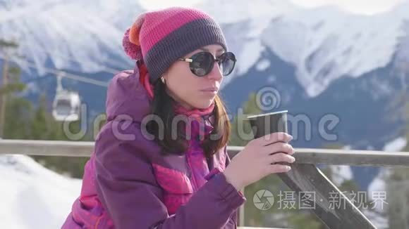 女人在山上的乡村木制露台上喝着温暖的茶。 女孩正在欣赏雪山的全景