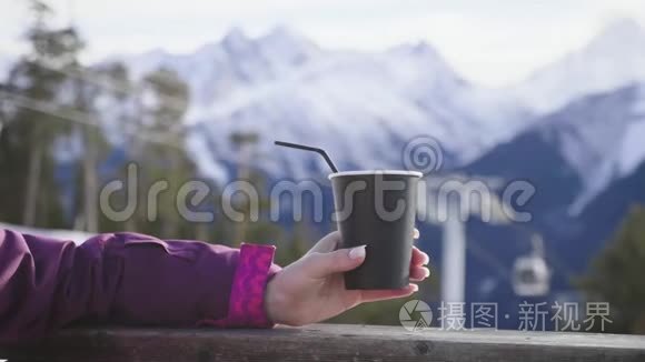 女人在山上的乡村木制露台上喝着温暖的茶。 女孩正在欣赏雪山的全景