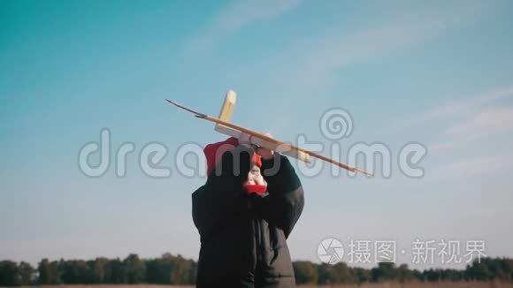 快乐的小男孩在日落时在大自然中玩木飞机。 孩子拿着一架木飞机梦想成为一个