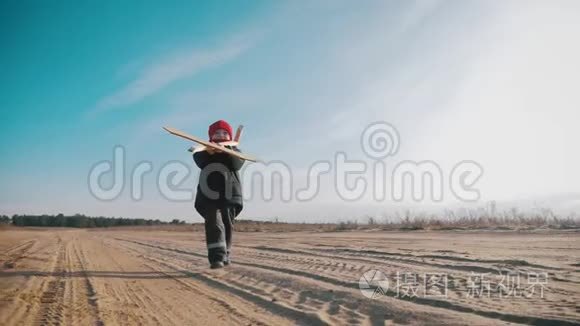 快乐的小男孩在日落时在大自然中玩木飞机。 孩子拿着一架木飞机梦想成为一个