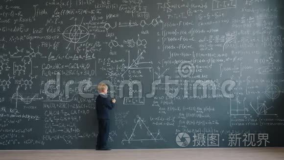 聪明的小男孩在学校的大黑板上缓慢地书写方程式