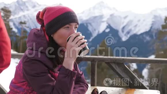 女人在山上的乡村木制露台上喝着温暖的茶。 女孩正在欣赏雪山的全景