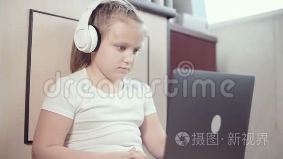 一个7岁的聪明的小女孩戴着白色耳机，手里拿着一台笔记本电脑，正在她的地板上推着