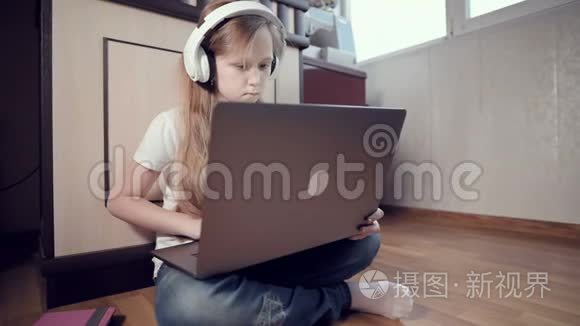 一个7岁的聪明的小女孩戴着白色耳机，手里拿着一台笔记本电脑，正在她的地板上推着