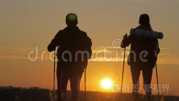 两个徒步旅行者的剪影带背包，从山顶欣赏日落景色。 享受日落美景