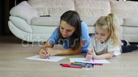 年轻的母亲画着彩色图画，可爱的女儿躺在温暖的地板上