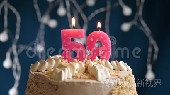 生日蛋糕上有59个数字粉红色燃烧蜡烛在蓝色的背景上。 蜡烛吹灭了。 慢速运动和特写镜头