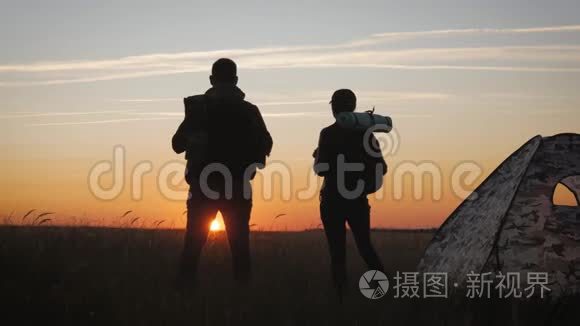 两个徒步旅行者的剪影带背包，从山顶欣赏日落景色。 享受日落美景