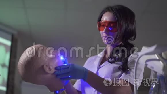 集中年轻的深色头发的女人使用牙科模特上的固化灯。 忙碌的高加索口腔医生的画像