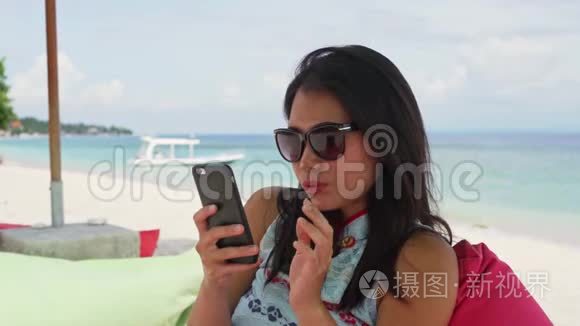 快乐的亚洲女人坐在海滩度假胜地的豆袋里，用手机自拍