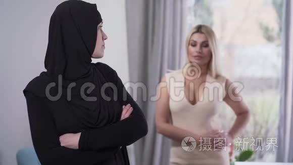 保守的穆斯林女人回头看现代白人女孩穿着坦率的衣服，转身离开。 适度的肖像