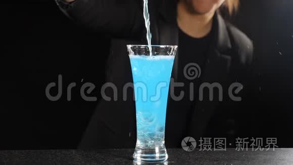 女调酒师在黑色背景下做蓝色冰鸡尾酒。 酒吧老板把明亮的蓝色酒倒入装满玻璃的玻璃中