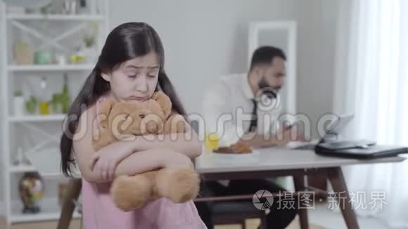 不高兴的小女孩回头看着忙碌的中东男人在笔记本电脑上打字，然后转身回到相机。 伤心的女儿