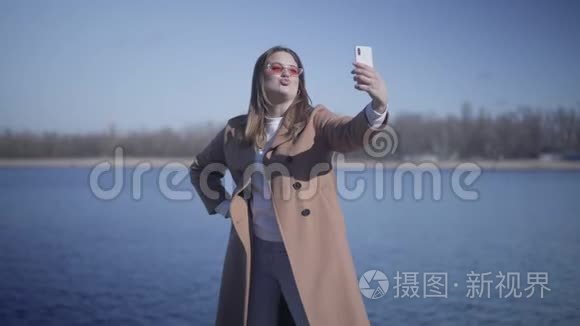 正面年轻女性在户外自拍相机上发送空气亲吻和鬼脸的肖像。 快乐的白人女孩