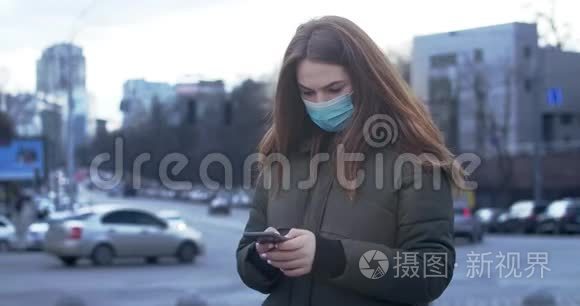 忧心忡忡的女人戴着防护面具站在城市街道上并使用智能手机的肖像。 忙碌的女孩在看新闻