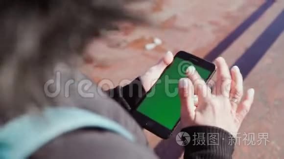 女孩手里拿着一部智能手机，手里拿着一个绿色的屏幕，在手机里沿着街道攀爬。 对Steadicam的射击