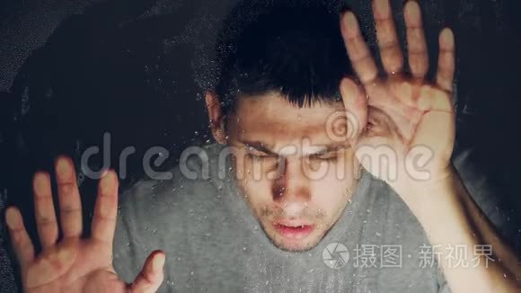 英俊的白人在磨砂玻璃后面看着里面。 男人抑郁。 上锁了，`不能出去