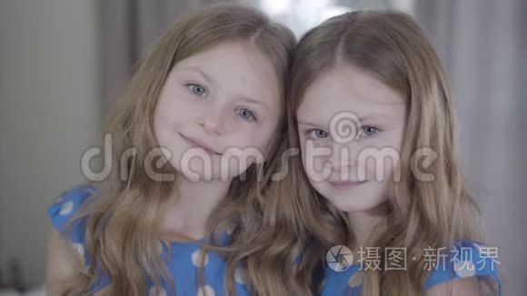 美丽的双胞胎姐妹在室内摆姿势的肖像。 冷静的孩子看着相机，微笑着。 两个快乐女孩