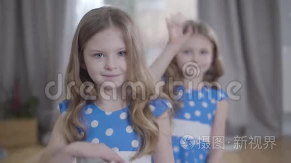 两个白人黑发双胞胎在镜头前挥手。 可爱的快乐姐妹穿着蓝色点缀的裙子享受免费