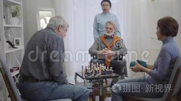年轻女性志愿者在养老院照顾三名退休人员。 年长的白人男子下棋，老妇人