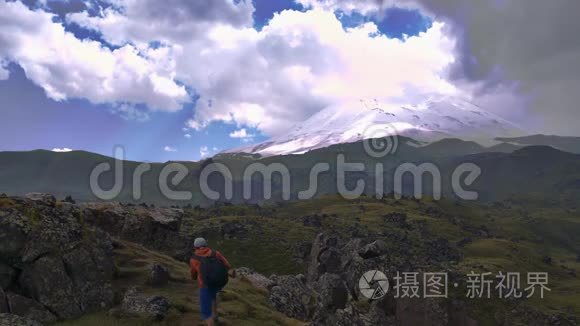 一个带着徒步旅行背包的人在美丽的风景背景上爬上了山，那里有高高的悬崖和云彩。 埃尔布鲁斯